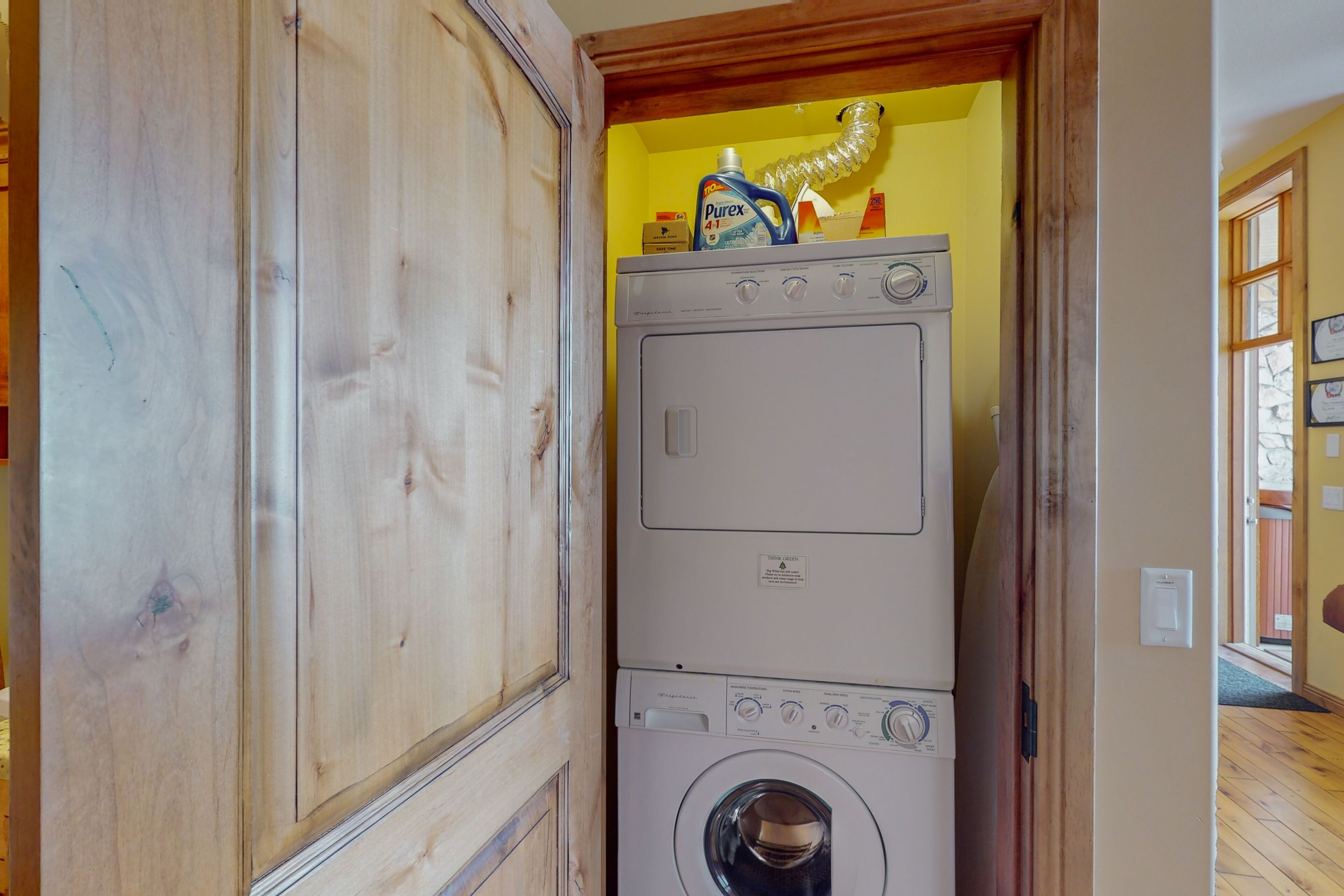 Une buanderie avec des machines à laver et des sèche-linge superposés, un meuble en bois et un mur jaune.