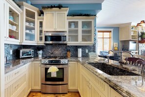 A kitchen with white cabinetry, a granite countertop, a built-in oven, a microwave, and a gas stove. - Aspens by Okanagan Premier (Beaverdell)