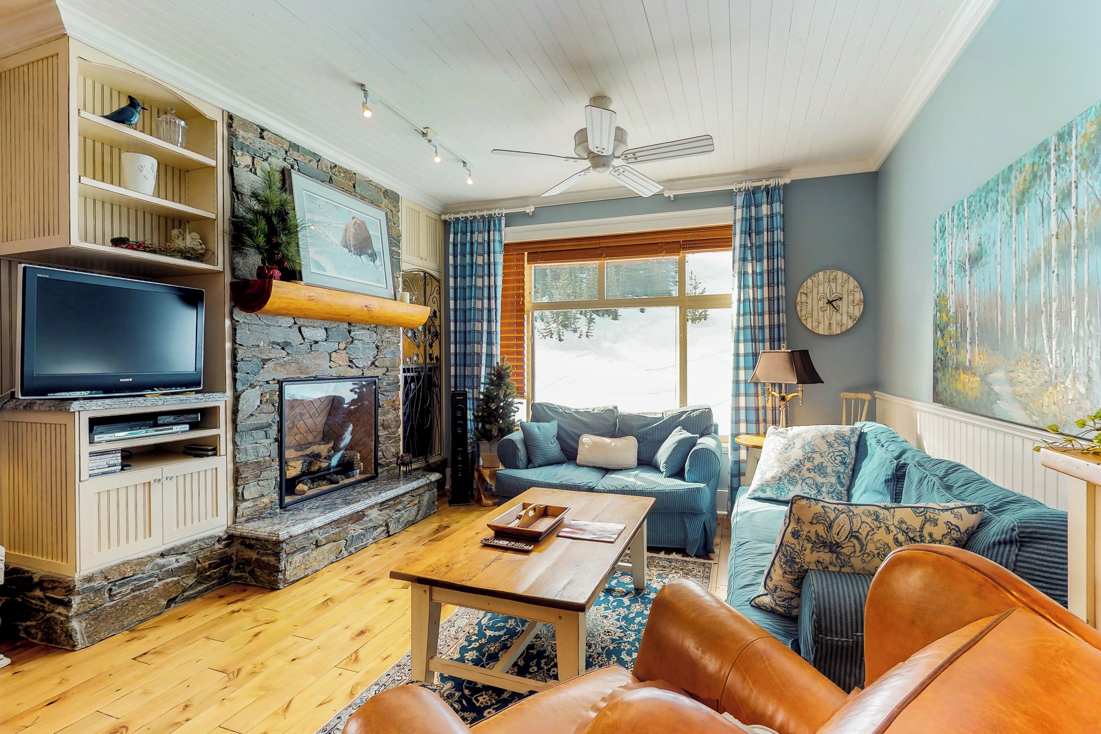A cozy living room with a stone fireplace, a television, a blue sofa, and a coffee table.