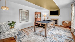 A living room with a pool table, a sofa, a television, and a fireplace. - Backyard Pool - Hot Tub - Game Room (Akron)