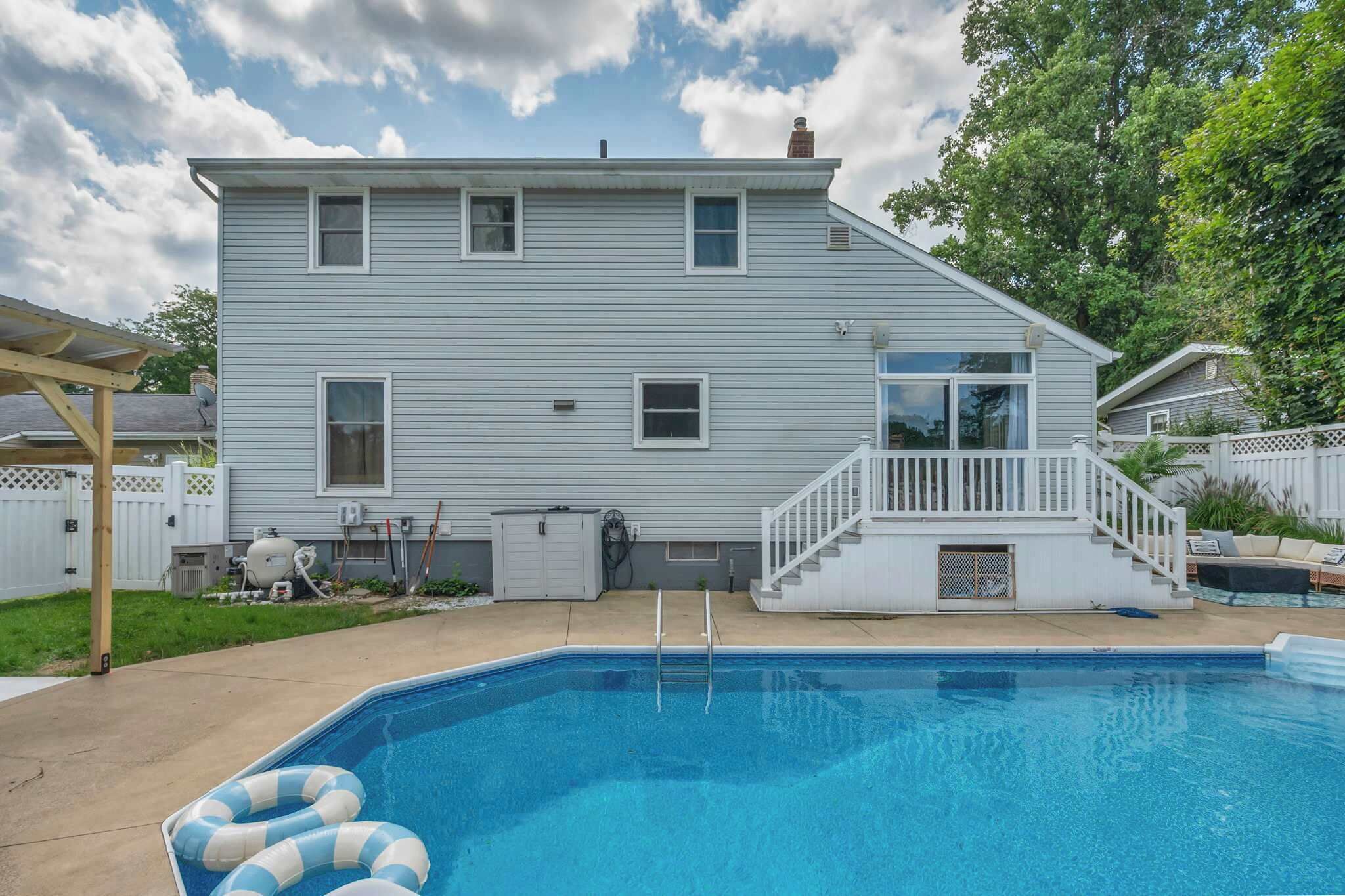 A two-story house with a swimming pool, a covered patio, and a fenced backyard.