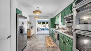 Uma cozinha com armários verdes, eletrodomésticos de aço inoxidável e um tapete estampado no chão.