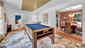 A pool table in a room with a dining area, a staircase, and a view of the outdoors. - Backyard Pool - Hot Tub - Game Room (Akron)