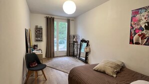 A bedroom with a bed, a chair, a desk, a window with curtains, and a door leading to a balcony.
