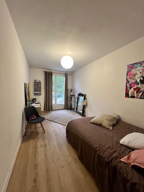 A bedroom with a bed, a chair, a desk, a window with curtains, and a door leading to a balcony. - Olivade: From the Countryside to the City (Aix-en-Provence)