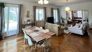 A spacious living area with a wooden herringbone floor, a dining table with chairs, a sofa, a pool table, and a television.
