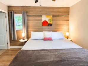 Een slaapkamer met een houten wand, een bed met wit bedlinnen, twee bedlampen en een raam met gordijnen.