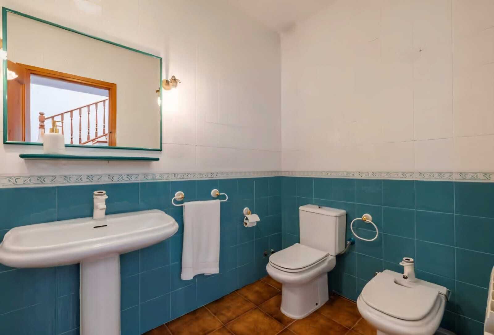 Une salle de bain équipée d’un lavabo, de deux toilettes, d’un miroir et d’une fenêtre donnant sur un escalier.
