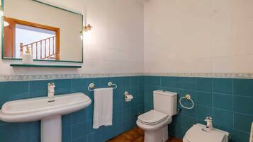 Un baño con lavamanos, dos inodoros, un espejo y una ventana que da a una escalera.