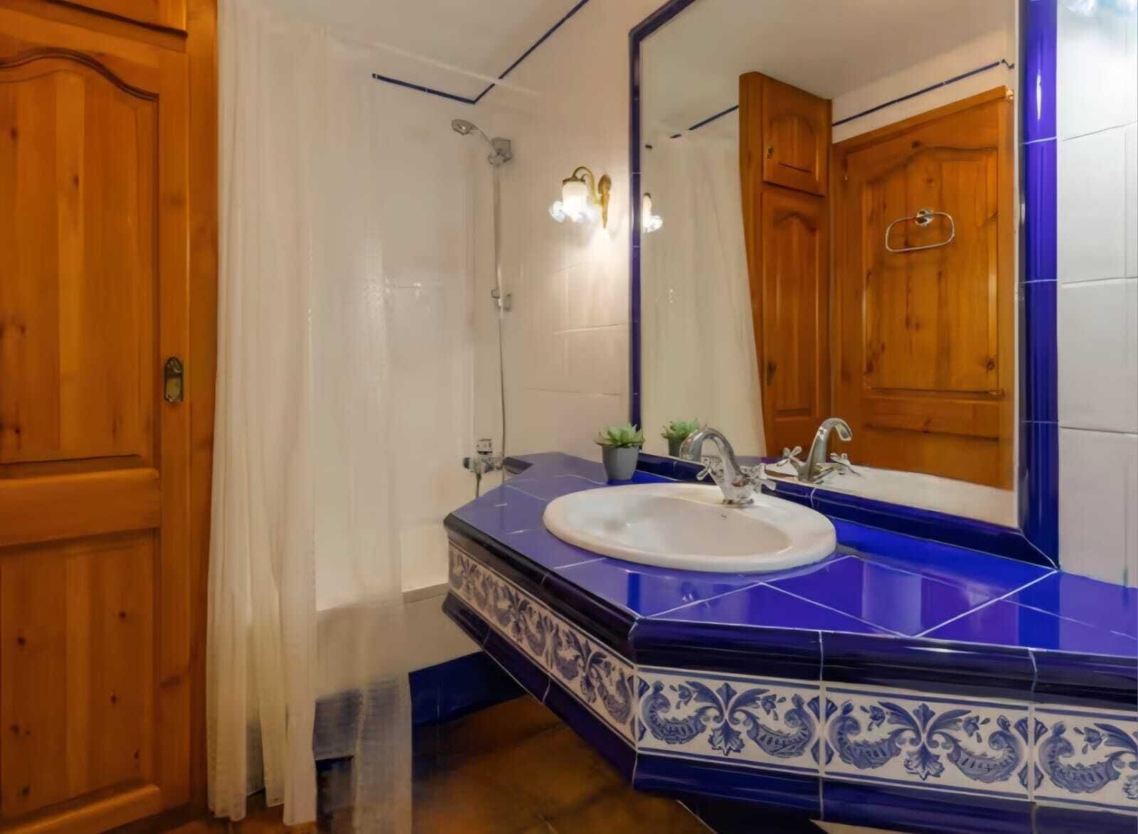 Ein Badezimmer mit einem blauen Fliesenbecken, einer Holztür und einem Duschbereich.
