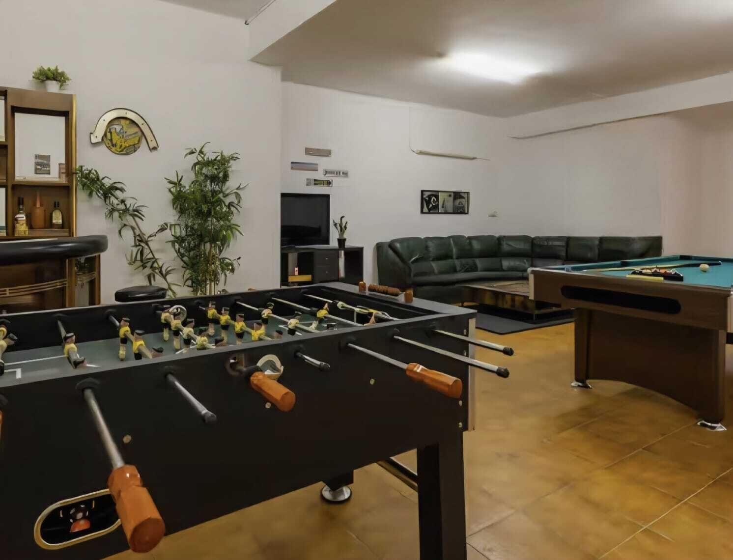 Una habitación con mesa de futbolín, mesa de billar, sofá y televisor.