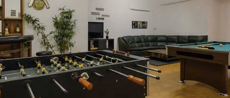 Una habitación con mesa de futbolín, mesa de billar, sofá y televisor.