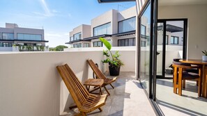 A balcony with wooden chairs, a dining table, and a potted plant.