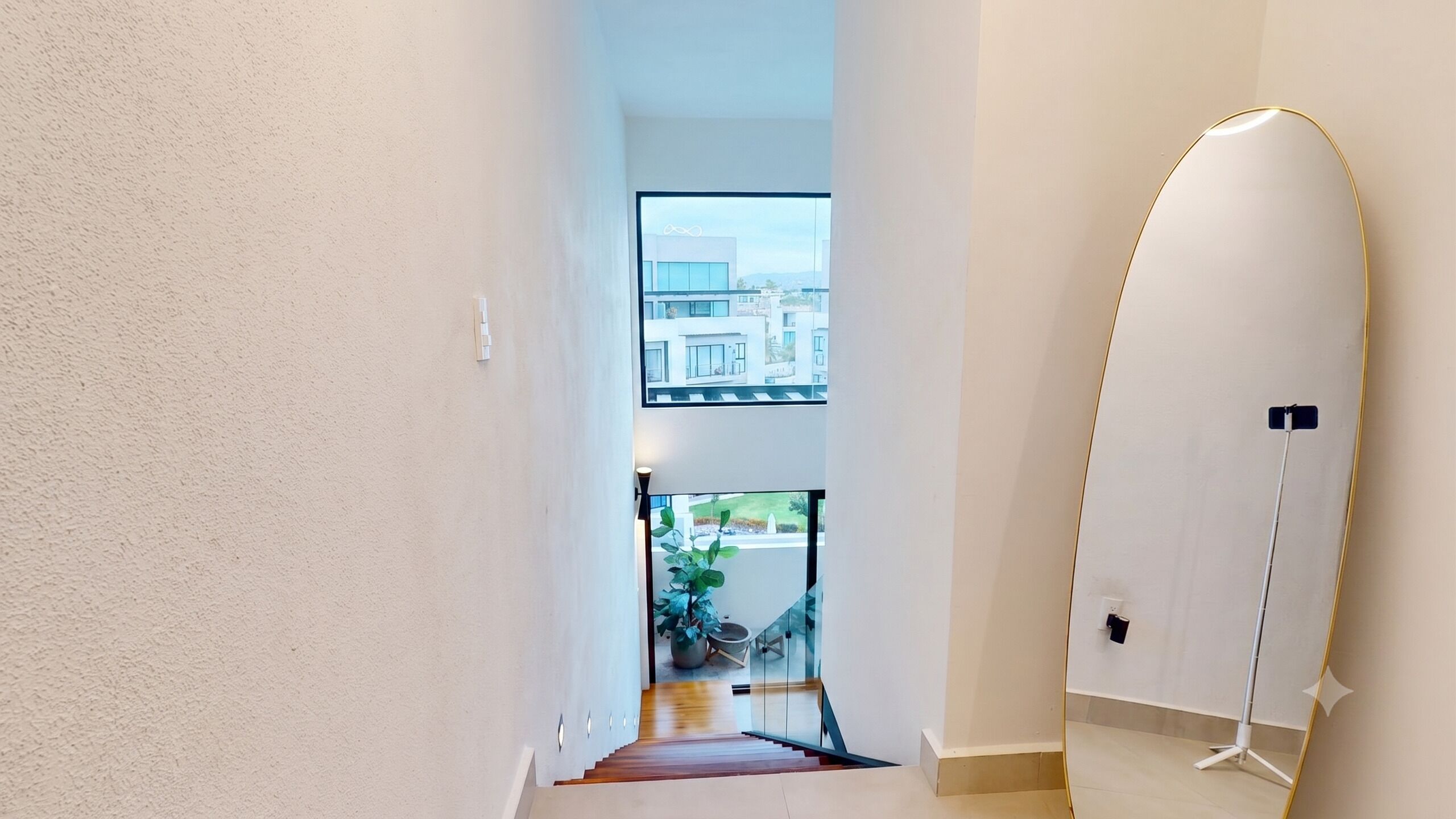 A hallway with a view of a modern building, a potted plant, and a standing lamp.