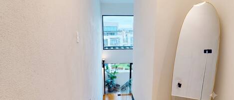 A hallway with a view of a modern building, a potted plant, and a standing lamp.
