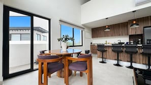 A modern kitchen with a bar area, large windows, and a dining set.