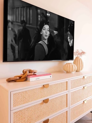 Ein an der Wand befestigter Fernseher, eine weiße Kommode mit Schubladen und ein rosafarbenes Buch mit dem Titel 'at 100'.