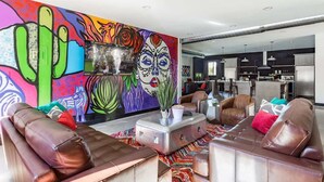Un salon avec des canapés en cuir, une fresque murale colorée et une cuisine en arrière-plan.