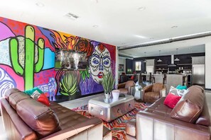 Ein Wohnzimmer mit Ledersofas, einem farbenfrohen Wandgemälde und einer Küche im Hintergrund.