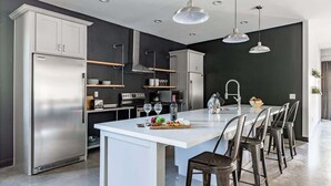 Une cuisine moderne dotée d’un îlot central, d’appareils électroménagers en acier inoxydable et de luminaires suspendus.