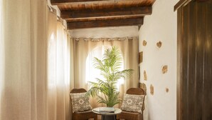 Ein Eckzimmer mit Fliesenboden, zwei Korbstühle mit gemusterten Kissen, ein kleiner runder Tisch und ein Blumentopf.