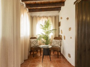 Ein Eckzimmer mit Fliesenboden, zwei Korbstühle mit gemusterten Kissen, ein kleiner runder Tisch und ein Blumentopf.