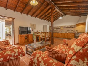 Ein Wohnzimmer mit Fernseher, Holzmöbeln und einer Küche im Hintergrund.