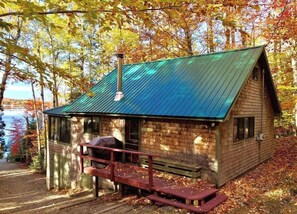 Une cabane avec un toit en métal, une terrasse en bois et une vue sur un lac.
