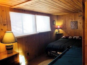 Un dormitorio de cabaña de madera con una cama, una mesita de noche, una lámpara y una ventana.