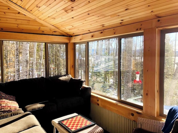 Una habitación acogedora con techo de madera, ventanas amplias, un sofá negro y un tablero de ajedrez.