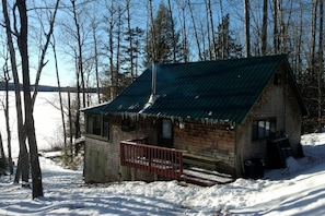 A cabin with a green roof, a wooden deck, and a snow-covered ground.