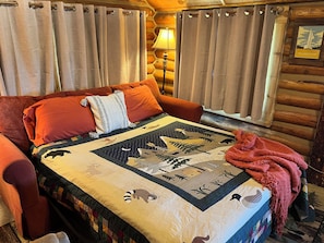 Ein Blockhauszimmer mit einem Bett, Vorhängen, einer Lampe und einer Decke mit Tiermotiven.