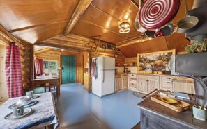 A rustic kitchen with wooden cabinets, a refrigerator, and a dining area with a table set for two.