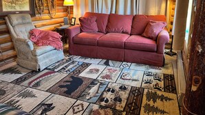 En stuga med träpanel på insidan, inredd med en röd soffa, en vadderad fåtölj, en mönstrad matta och ett trätak.