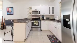 Una cocina moderna con armarios blancos, electrodomésticos de acero inoxidable, un taburete de bar y suelo de baldosas.
