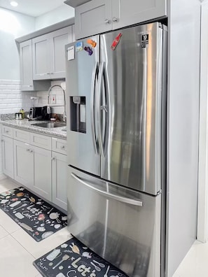 Ein Edelstahl-Kühlschrank in einer modernen Küche mit weißen Schränken und einer Arbeitsplatte aus Granit.