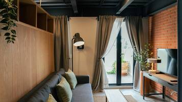 Un salon moderne avec un canapé, un bureau doté d’un téléviseur et une grande fenêtre agrémentée de rideaux.