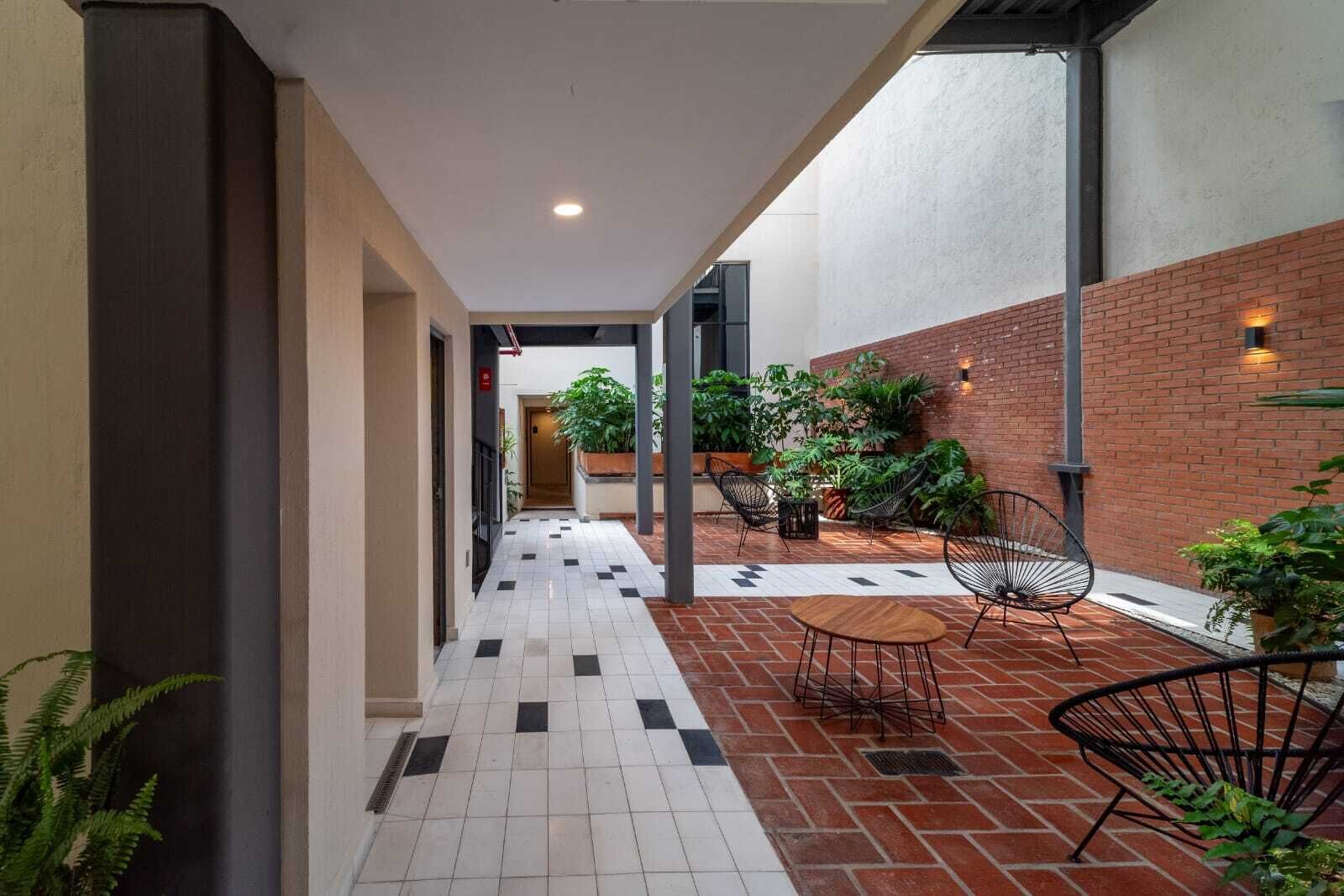 Un pasillo con suelo de baldosas, pared de ladrillo y mobiliario exterior con sillas y mesas.