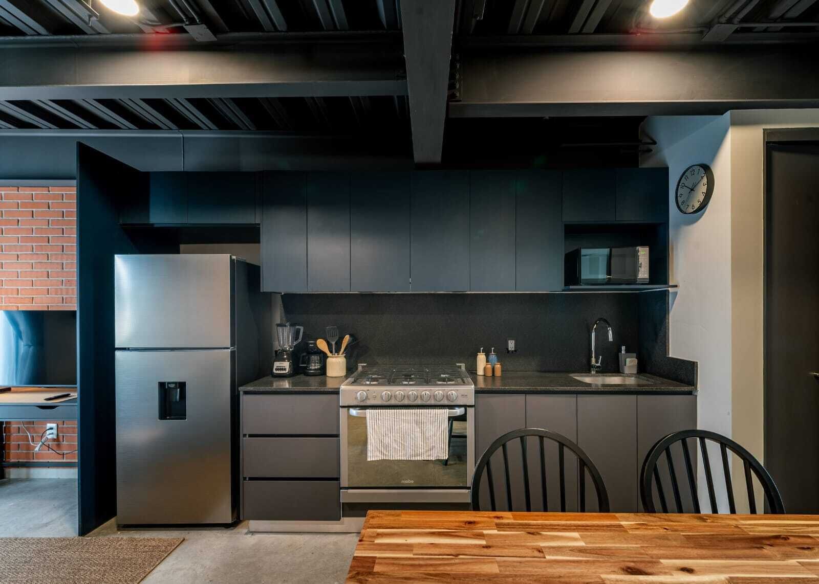 A modern kitchen with a stainless steel refrigerator, a built-in oven, and a microwave. There is a wooden dining table with chairs.