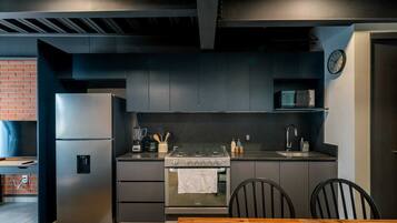 A modern kitchen with a stainless steel refrigerator, a built-in oven, and a microwave. There is a wooden dining table with chairs.