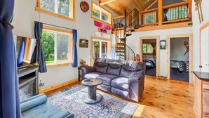 A spacious living room with a high ceiling, wooden beams, a fireplace, a sofa, and a staircase leading to an upper level.