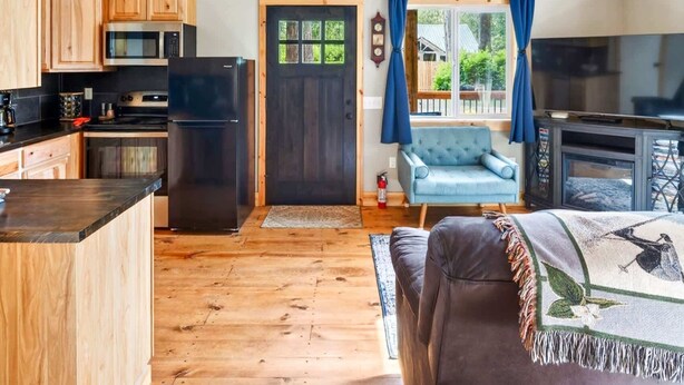 A spacious kitchen with wooden cabinets, a black refrigerator, and a dining area with a sofa and a television.