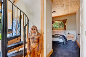 A wooden staircase leading to a bedroom with a bed, a nightstand, and a window with curtains. - Mt Hood Cabin, Hot Tub, Fire Pit, Dog-Friendly (Sandy)