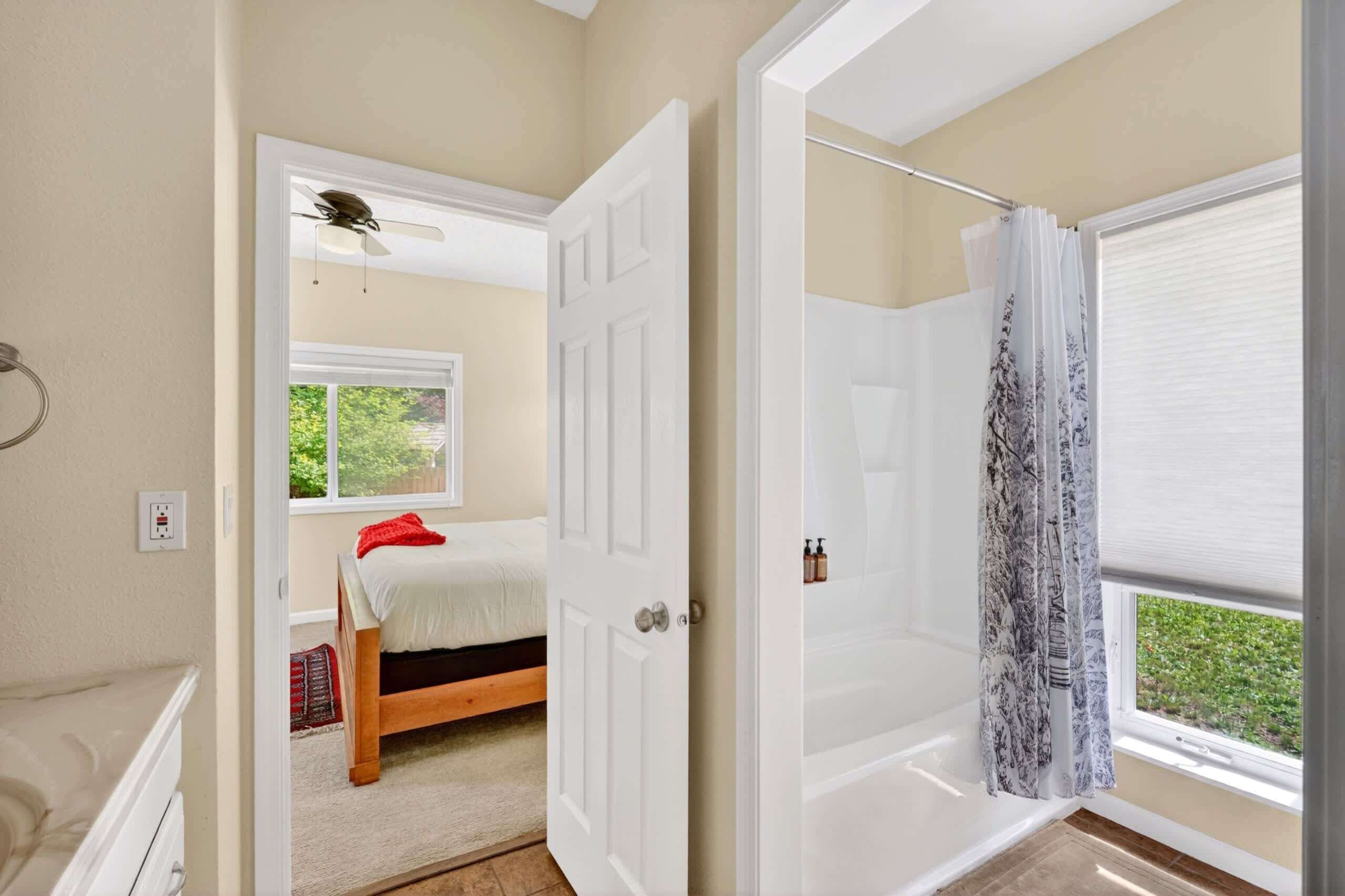 A bedroom with a bed, a ceiling fan, a window, and a shower area with a curtain.