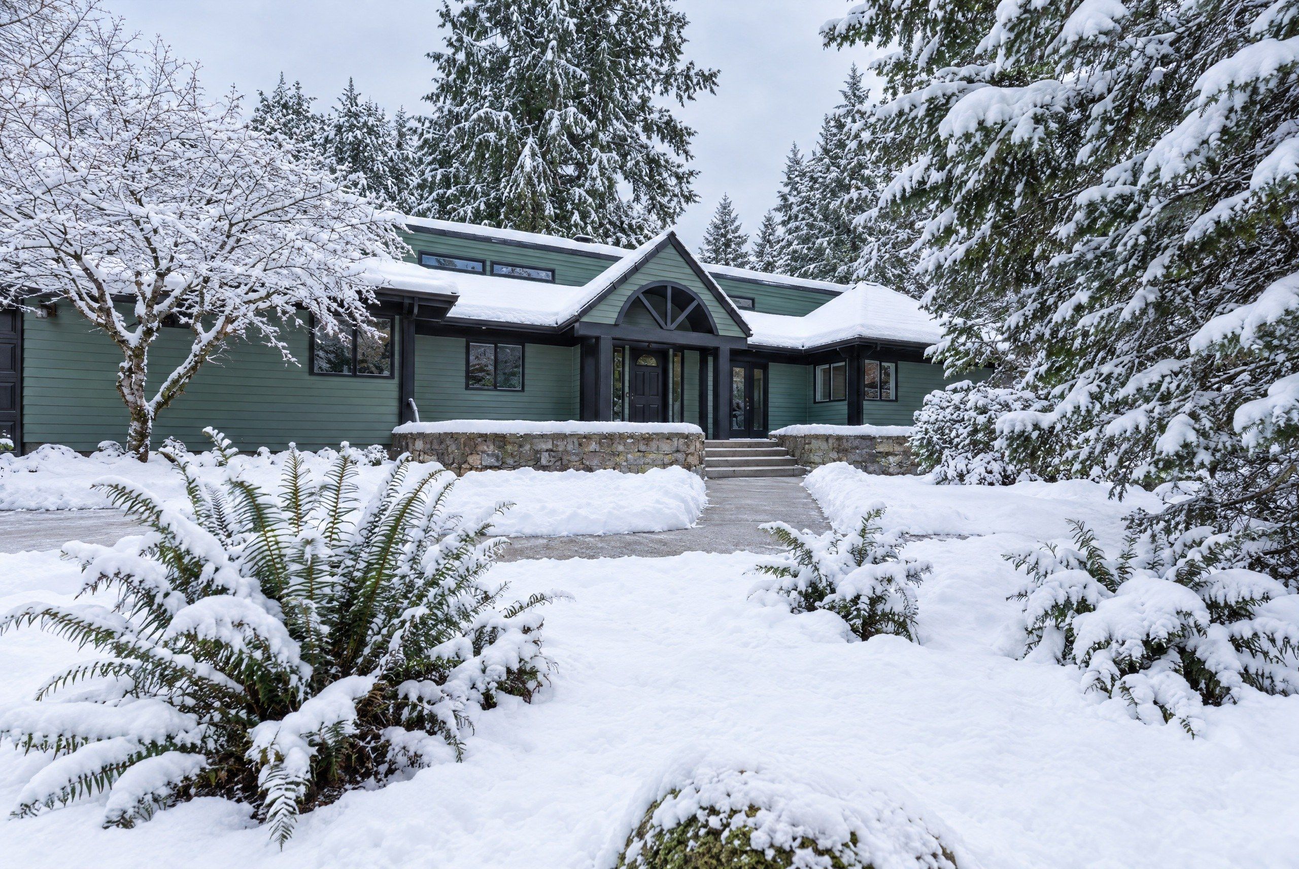 A two-story house with a stone foundation, a green exterior, and a snow-covered roof.