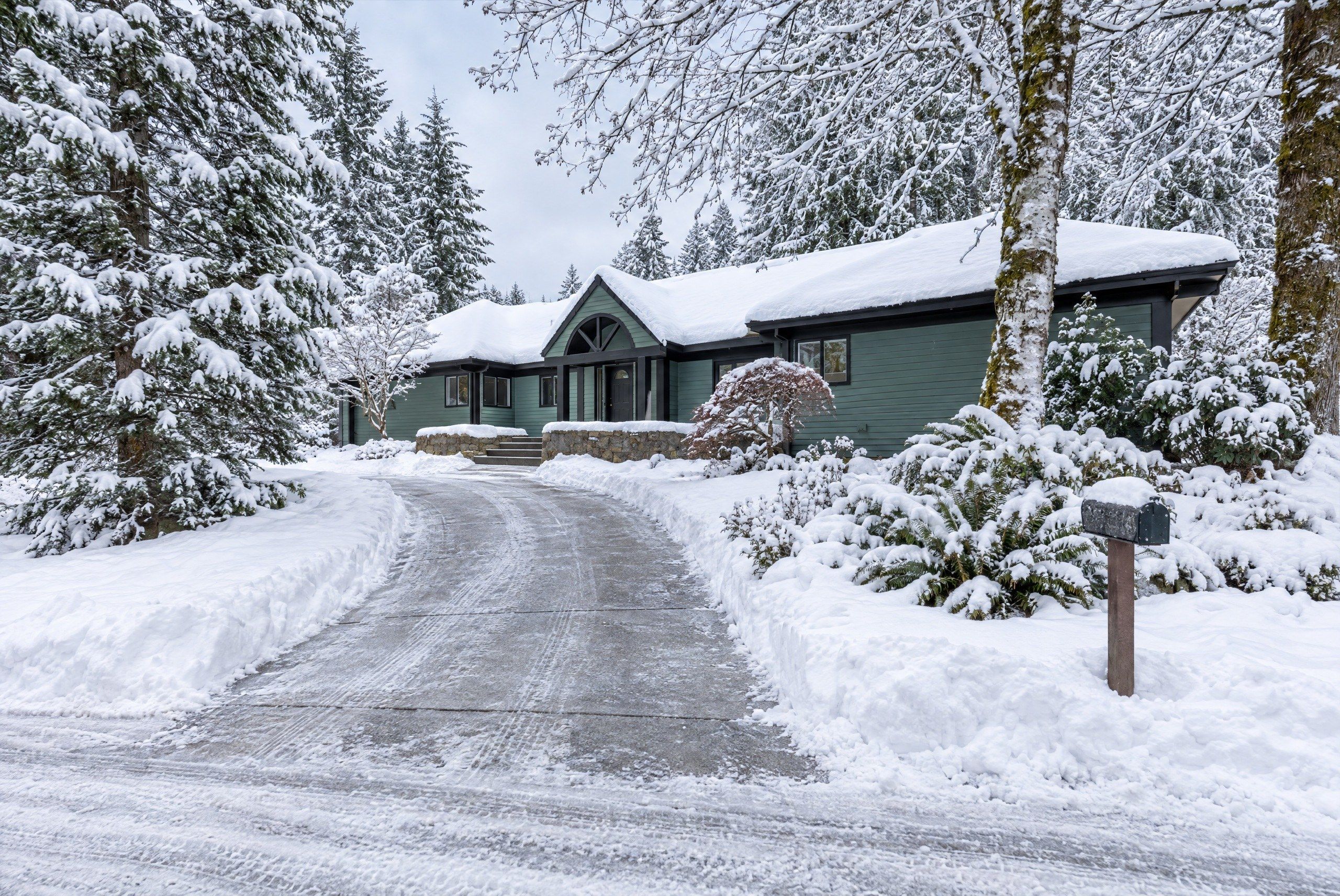 A snow-covered house with a driveway leading to the entrance.