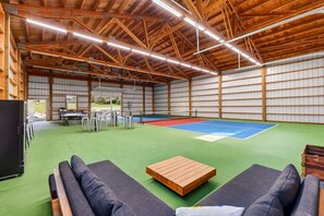 Una cancha deportiva interior con piso verde, una mesa de ping pong y zonas de estar.