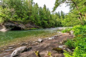 Une rivière qui traverse une zone boisée, avec des rives rocheuses et l’entrée d’une grotte.