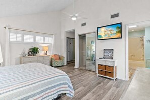 Ein Schlafzimmer mit einem Bett, einem Schminktisch, einem Sessel, einem Fernseher und einer Tür zu einem Badezimmer.