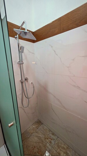 Eine Dusche mit Duschbrause und Reinigungsbürste, ein Eckfliesenmuster und ein Holzakzent an der Decke.